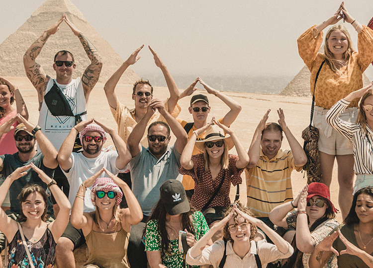 Group of Topdeck travellers in Egypt in front of the Pyramids posing for a photo using their arms to make pyramid shapes.